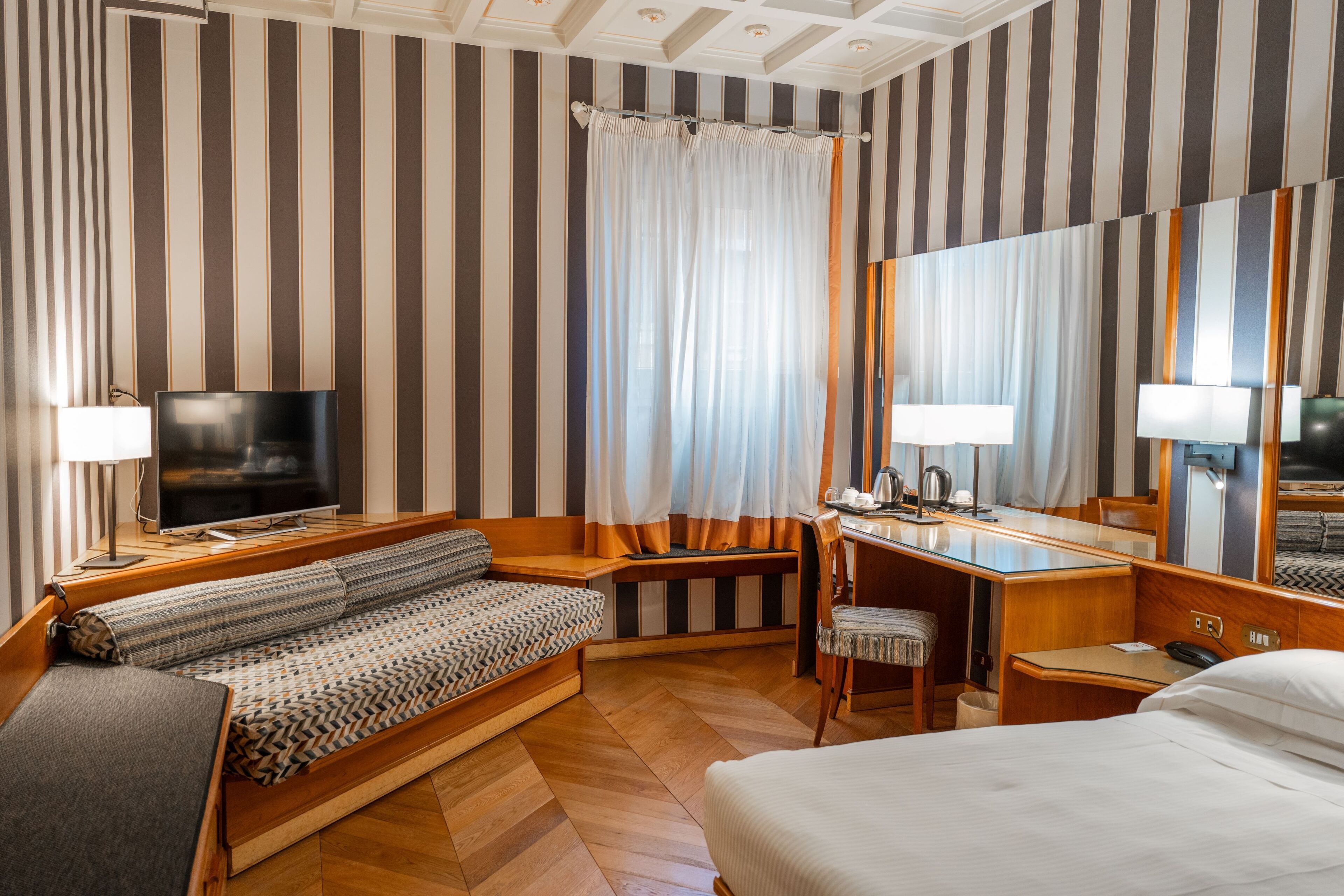 A hotel room with a large bed, a sofa, a desk, a chair, a television, and a large mirror.