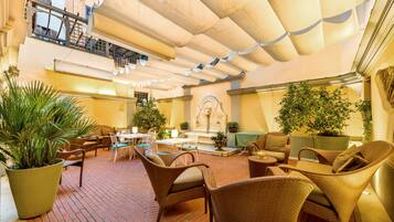 An indoor courtyard with wicker furniture, potted plants, and a fountain.