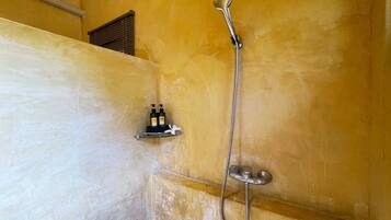 A shower with a handheld showerhead and a wall-mounted faucet. There are two bottles on a shelf beside the shower.