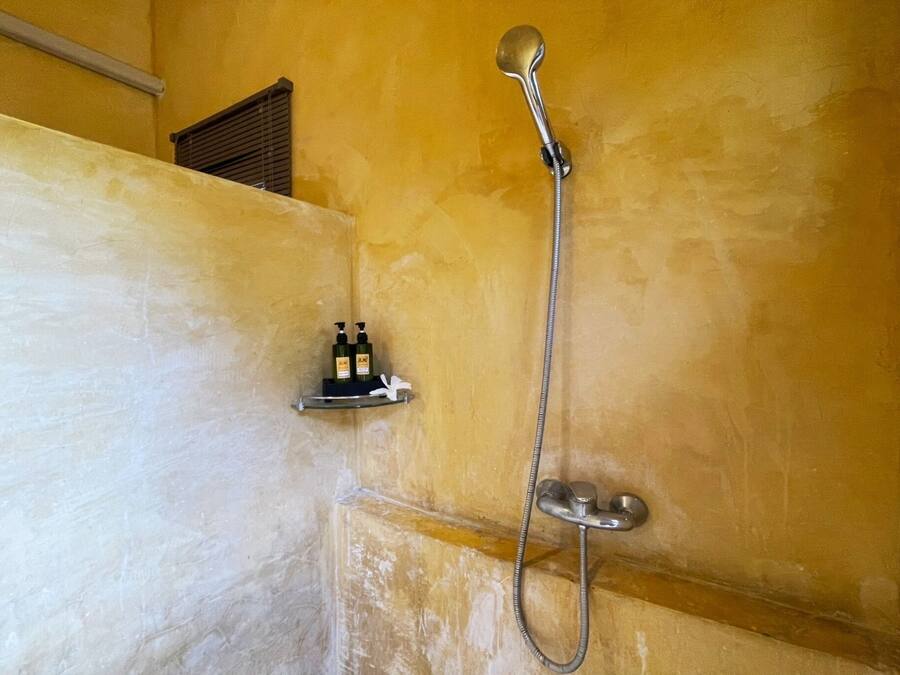 A shower with a handheld showerhead and a wall-mounted faucet. There are two bottles on a shelf beside the shower.