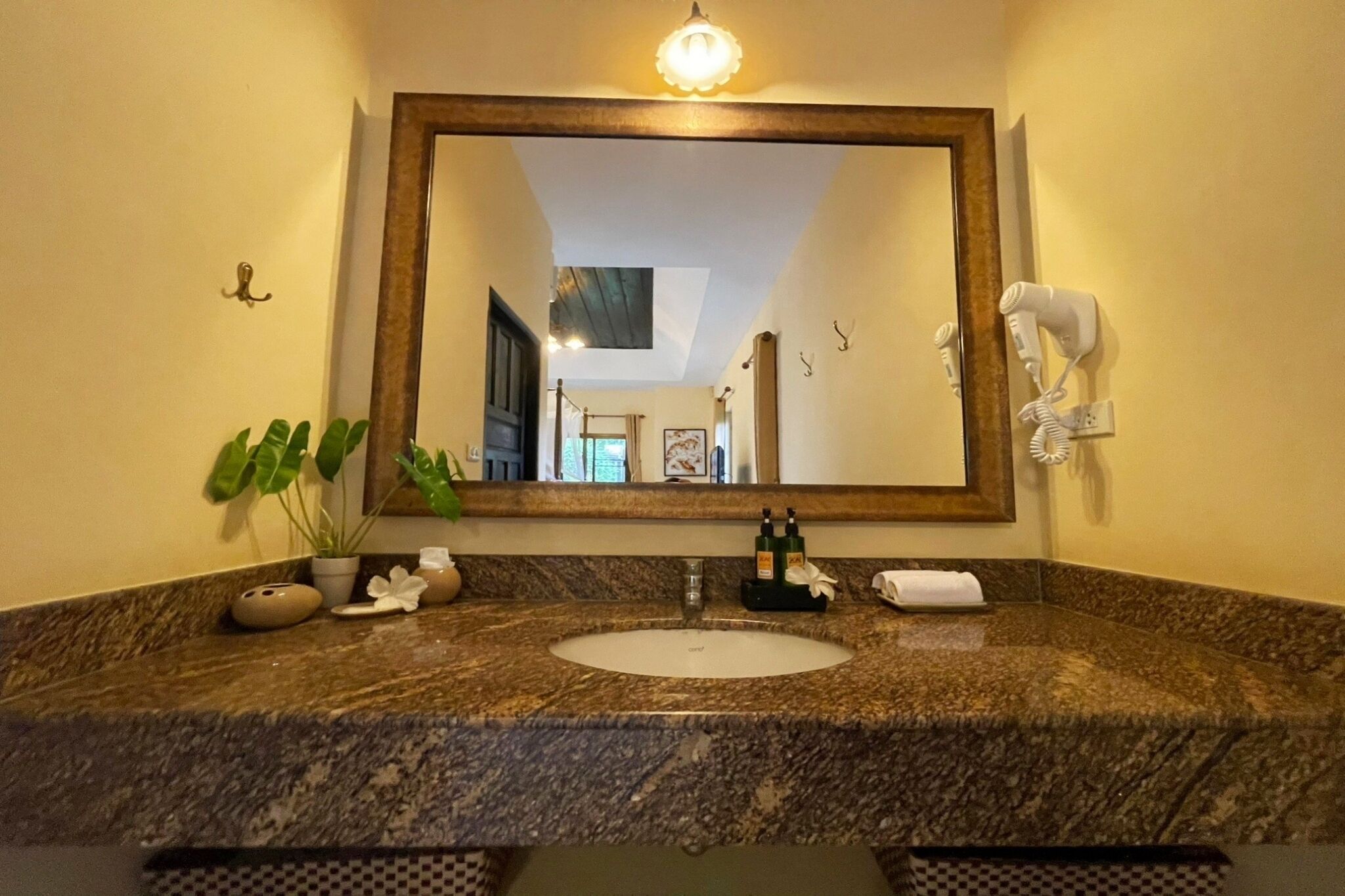 A bathroom with a marble sink, a large mirror, a hairdryer, and a potted plant.