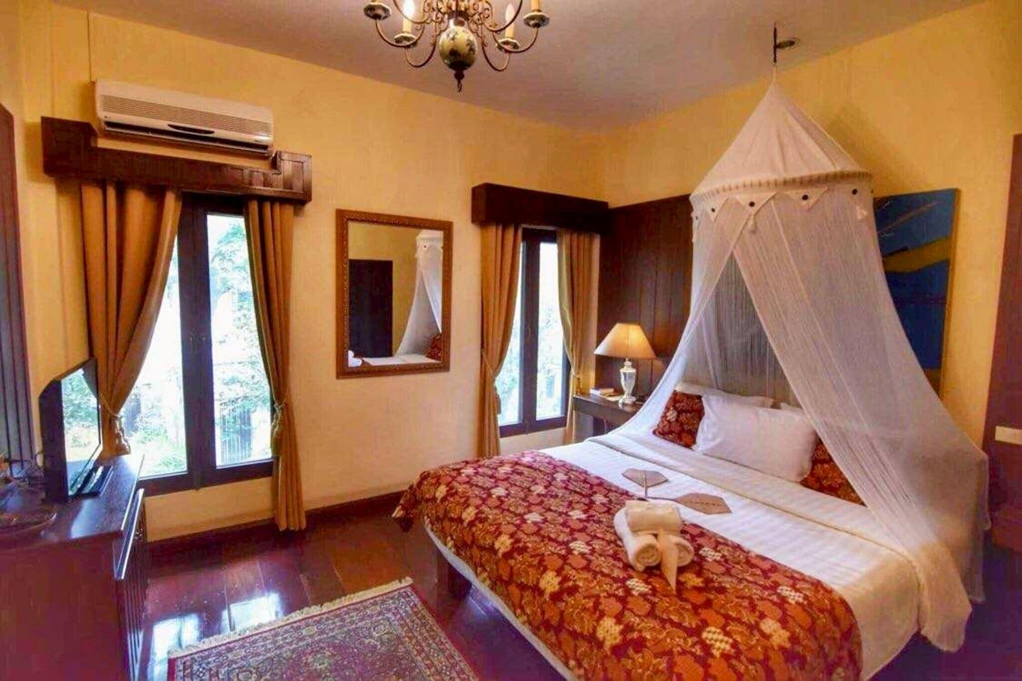 Hotelkamer met een bed, hemelbed, nachtkastje, lamp, spiegel en een airconditioning.
