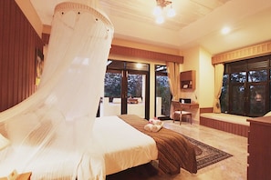 A bedroom with a bed, a desk, a chair, a large window, and a view of the outdoors. - Villa Khao Phaengma (Wang Nam Khiao)