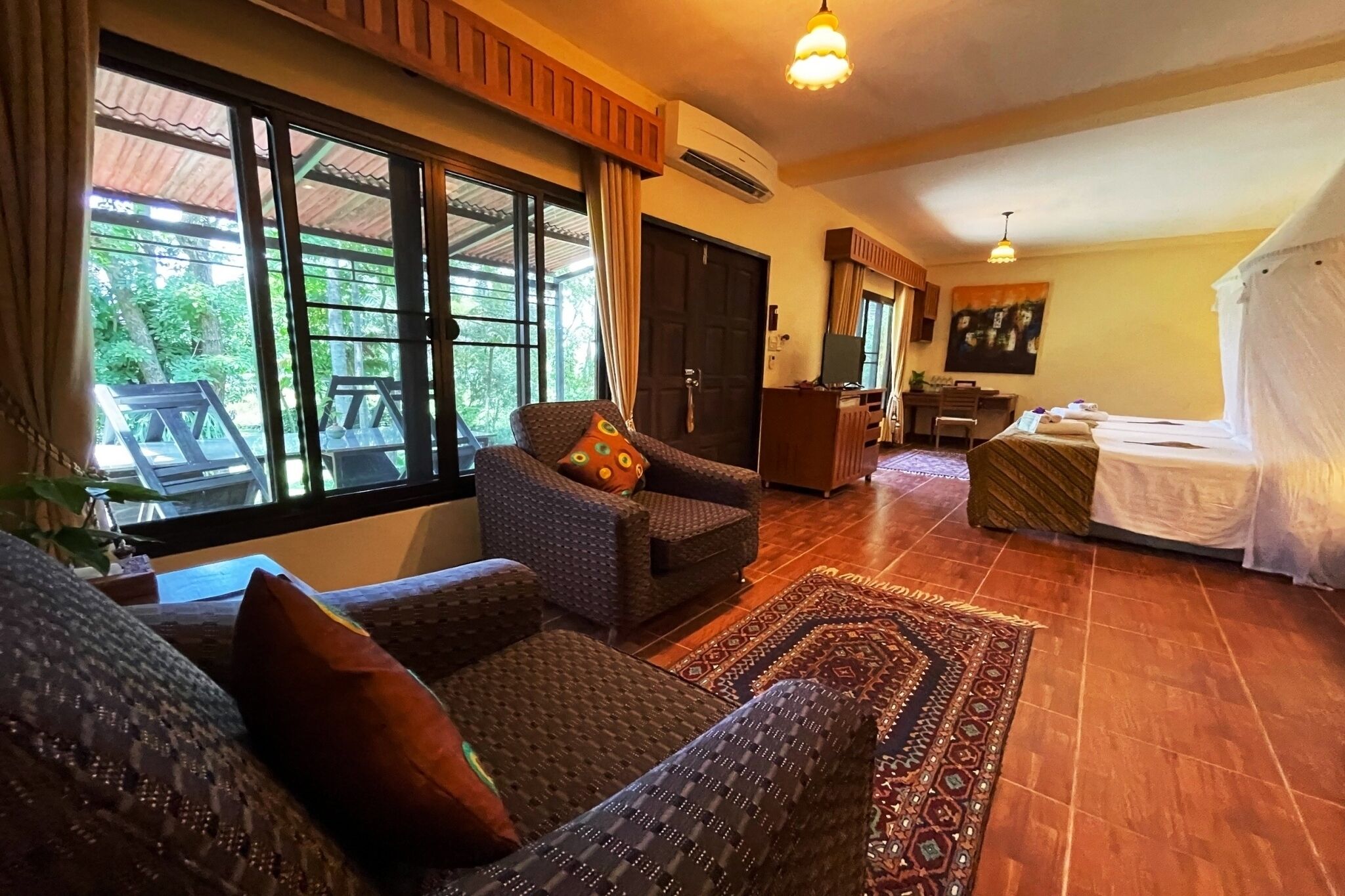 Una habitación con sofá, sillón y cama. Se ve un ventanal con vistas a zonas verdes.