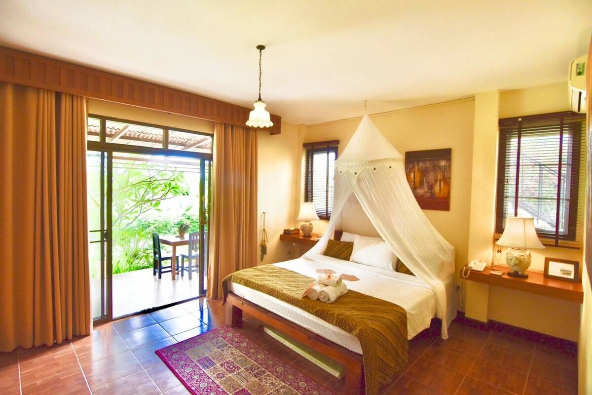 Une chambre à coucher comprenant un lit, une table de chevet, une commode, une fenêtre et une vue sur la verdure à l’extérieur.