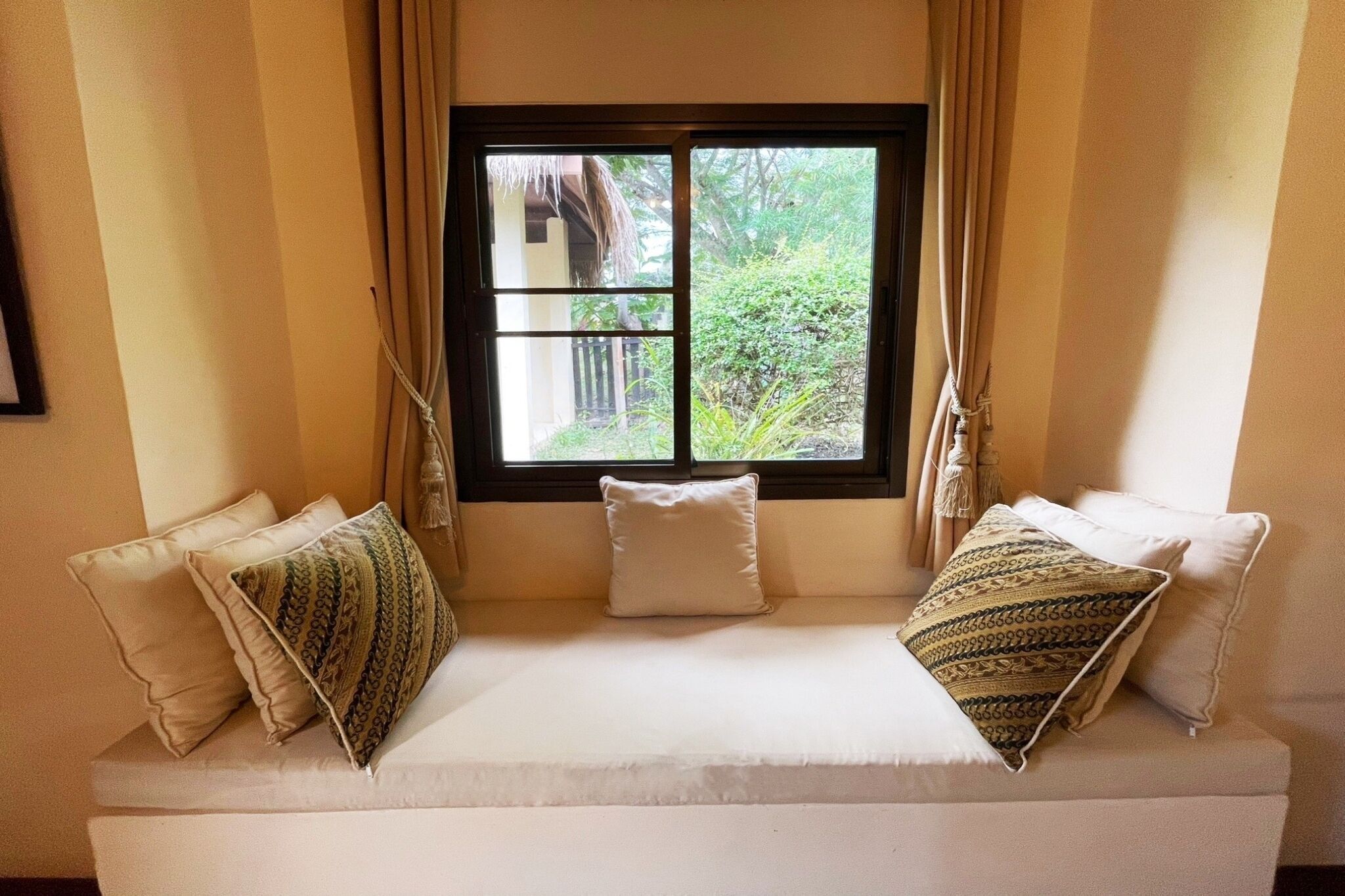 A room with a window, a sofa with cushions, and curtains.