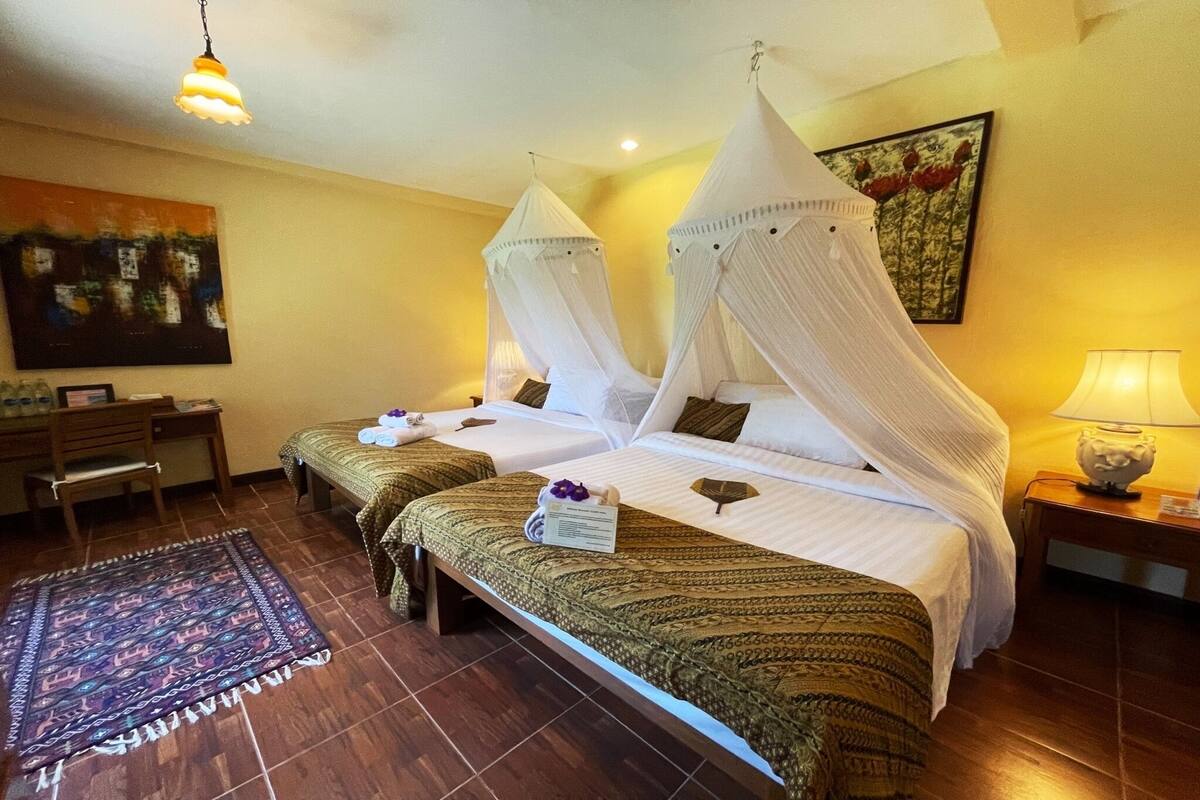 Une chambre d’hôtel avec deux lits, un bureau, une chaise, un tapis et un tableau au mur.