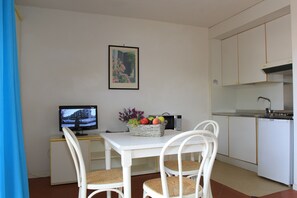 Cocina compacta con muebles blancos, microondas, lavamanos y comedor con mesa y sillas blancas.