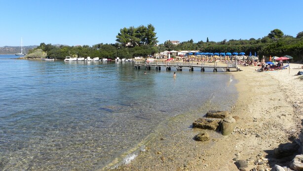 Una playa con agua cristalina, barcos y sombrillas.