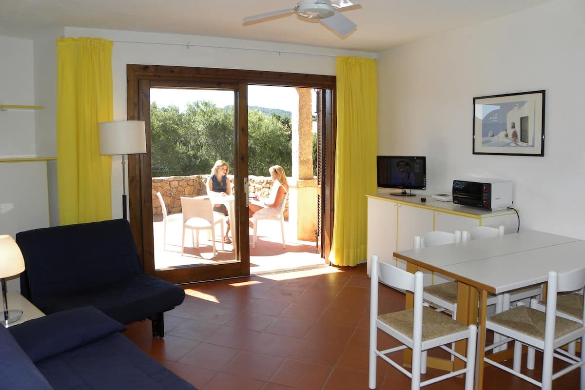 A room with a sofa, a dining table, chairs, a TV, and a ceiling fan.