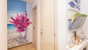 A hallway with a mural of a beach scene, a wooden door, and a shelf with books and decorative items. - La Loggia de' Banchi (La Spezia)