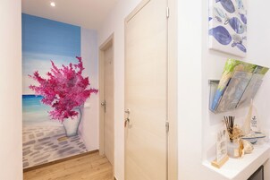 A hallway with a mural of a beach scene, a wooden door, and a shelf with books and decorative items.