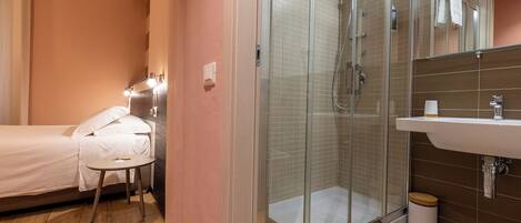 A hotel room with a bed, a round table, a glass-enclosed shower, and a sink with a mirror.