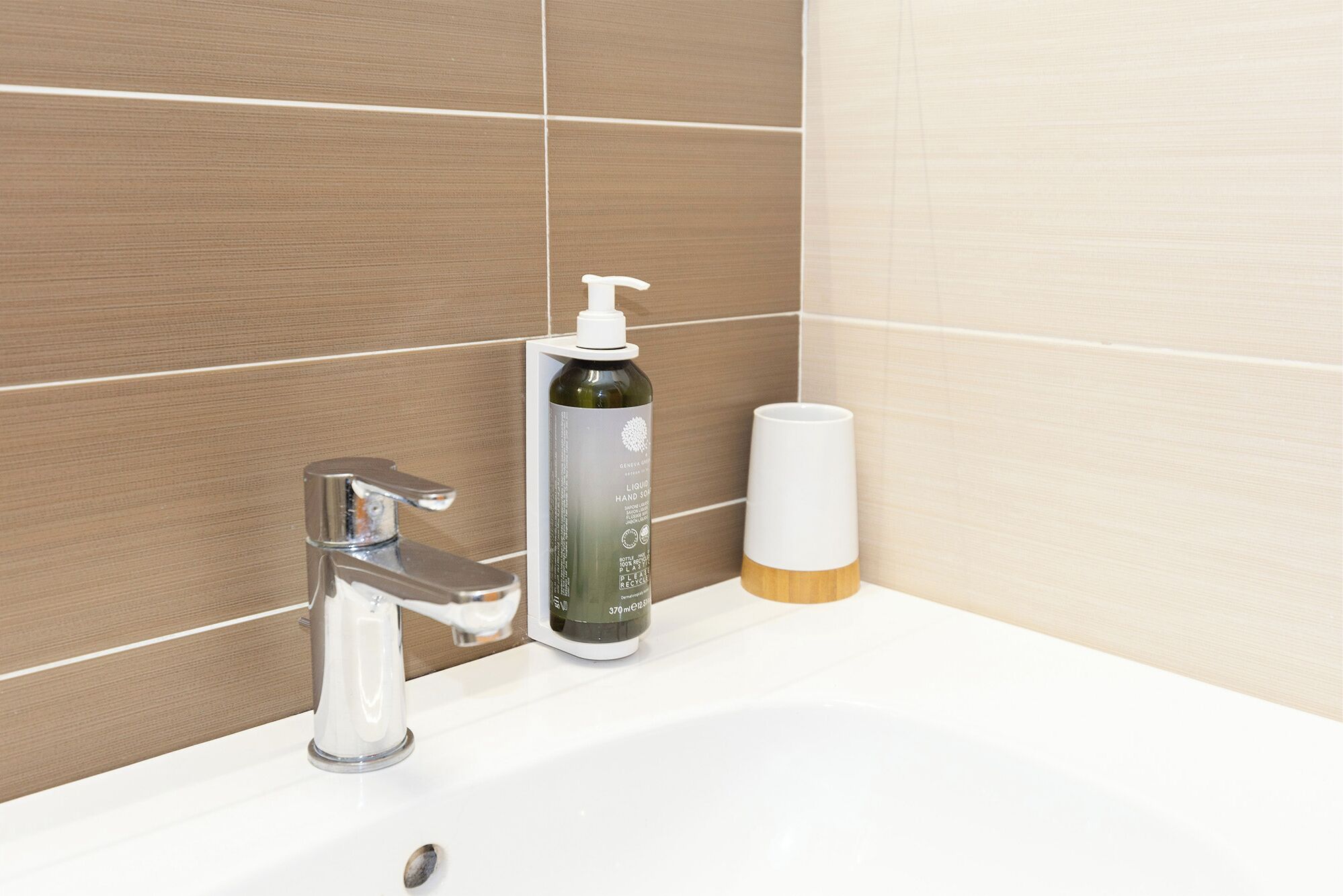 Un lavabo de salle de bain avec un robinet chromé, un flacon de savon liquide et un gobelet blanc.
