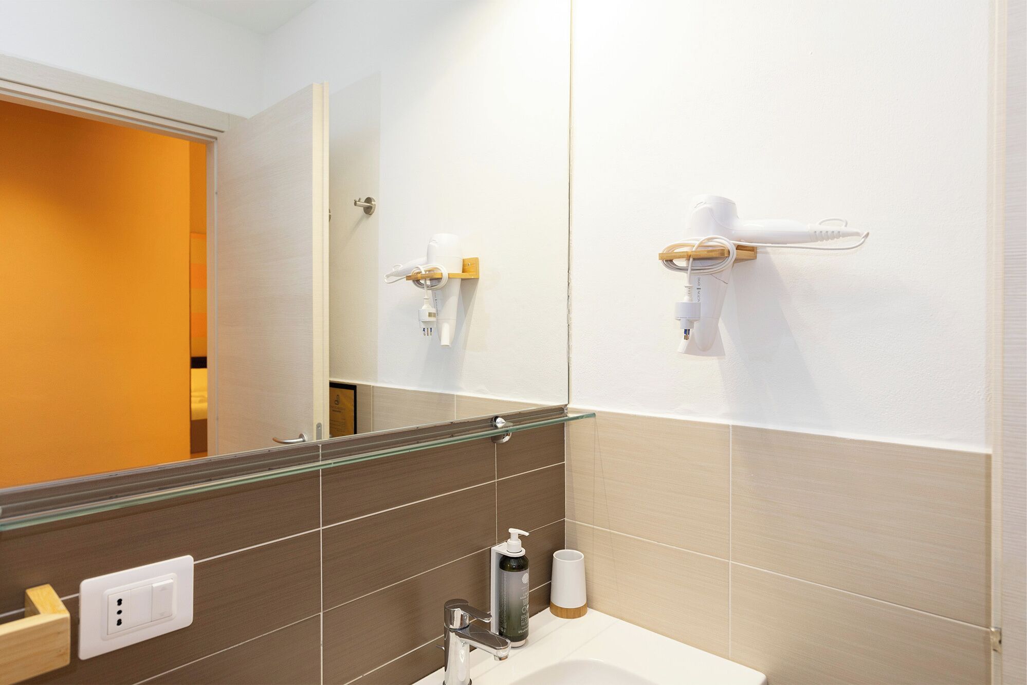 Un baño moderno con cabina de ducha de vidrio, un lavabo blanco y un secador de pelo montado en la pared.