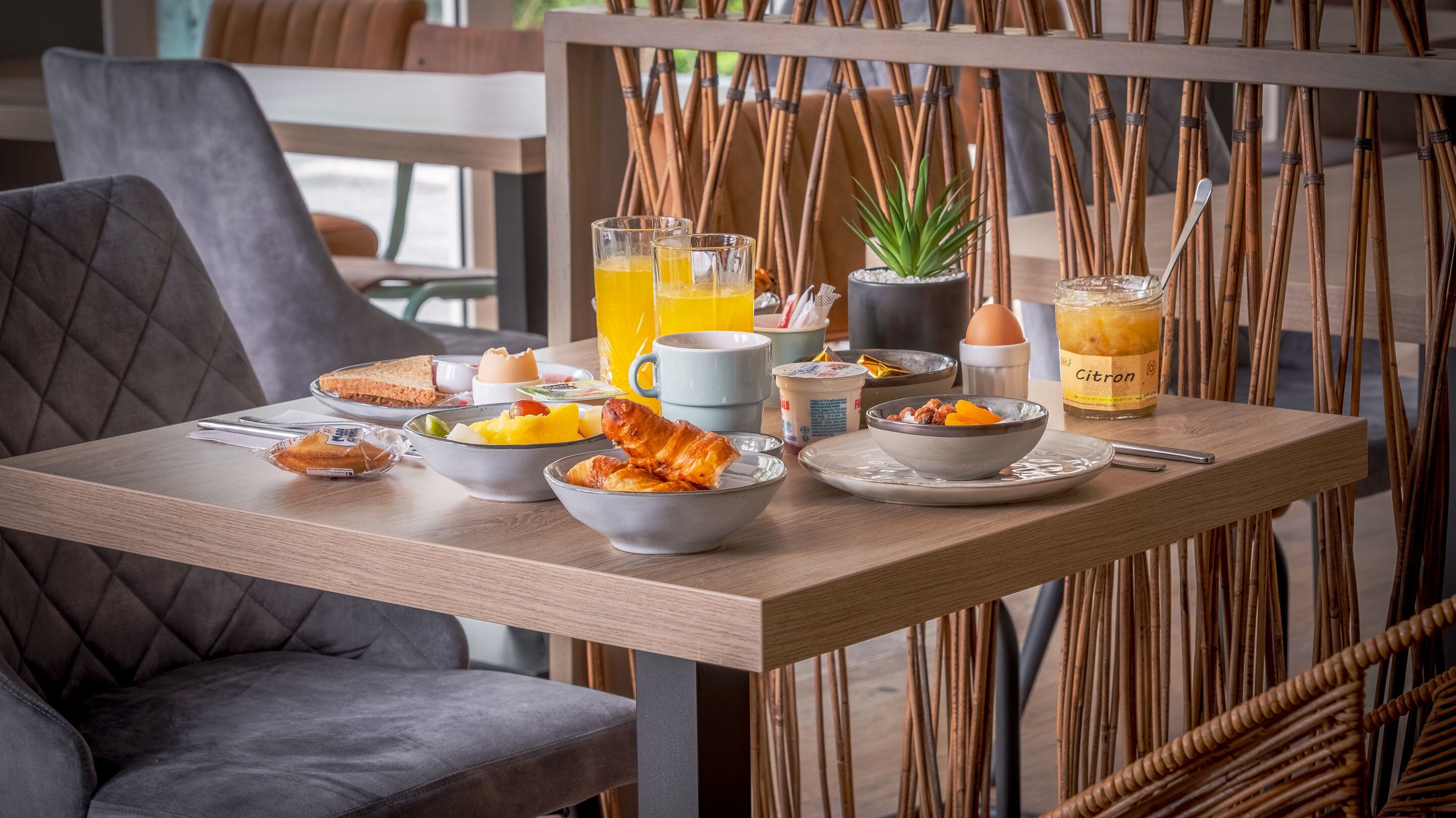 A breakfast table with various food items, a glass of orange juice, and a bottle of Citron.