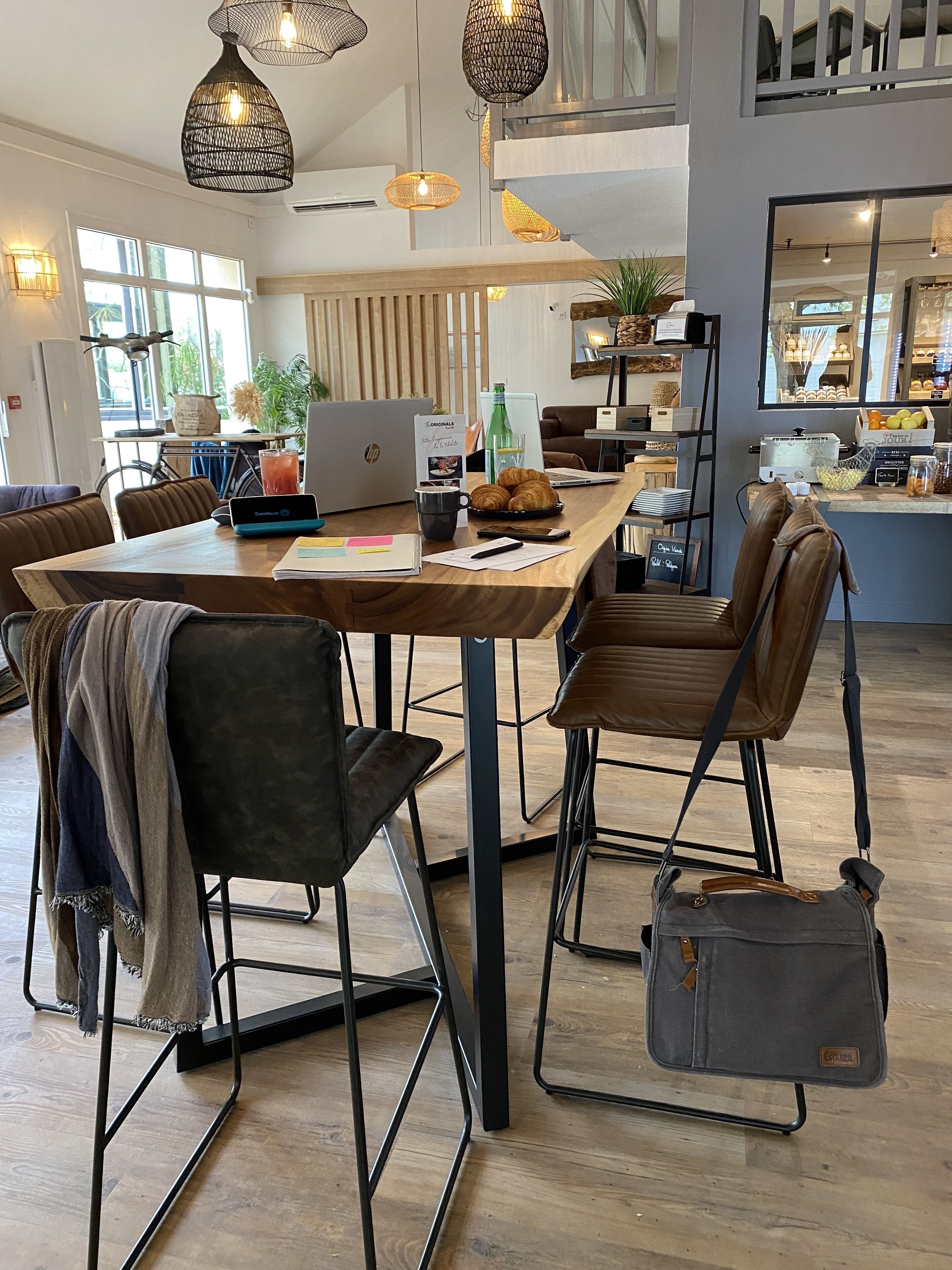 Un caffè moderno e luminoso con un tavolo in legno, poltrone in pelle e un laptop sul tavolo.