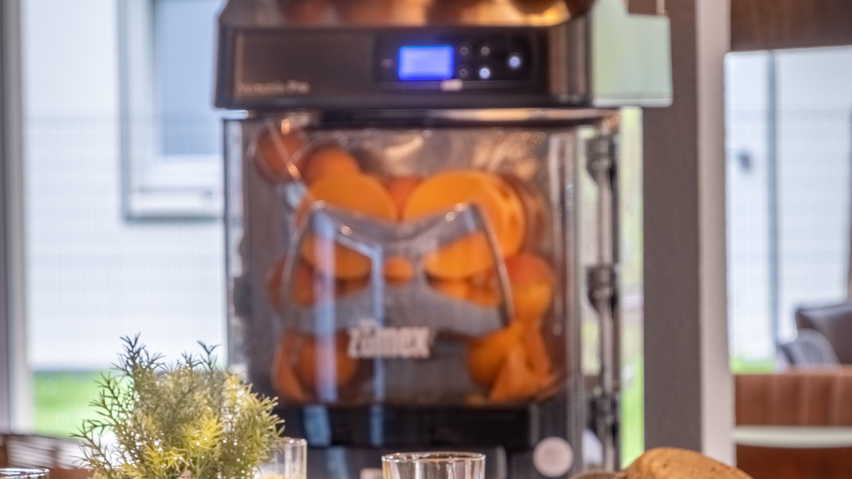 A coffee machine with a digital display, a glass container with orange slices, and a small plant on the table.