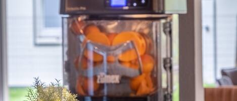 A coffee machine with a digital display, a glass container with orange slices, and a small plant on the table.