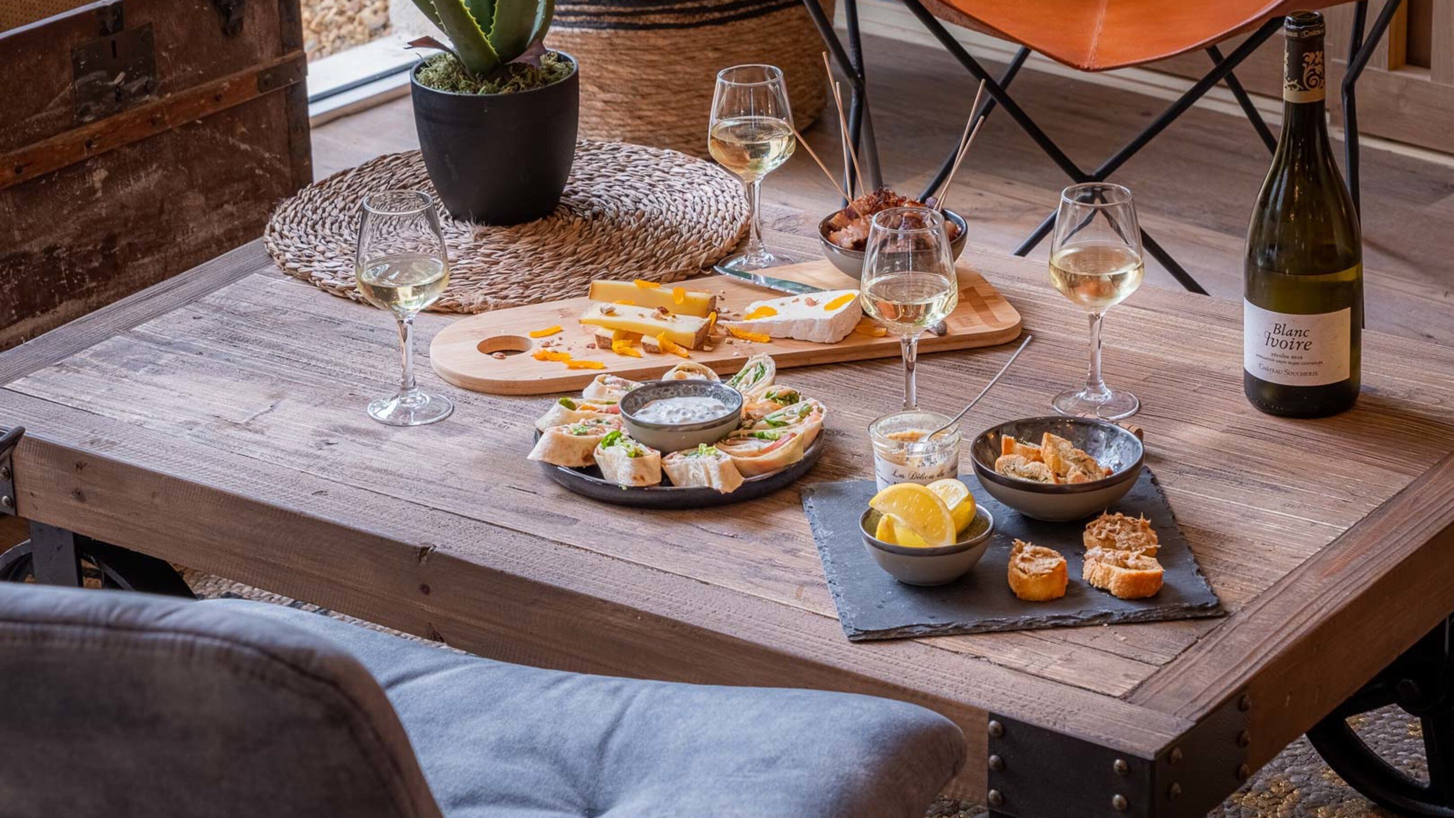 Una mesa de madera dispuesta con varios quesos, embutidos y copas de vino, evocando una experiencia gastronómica relajada.
