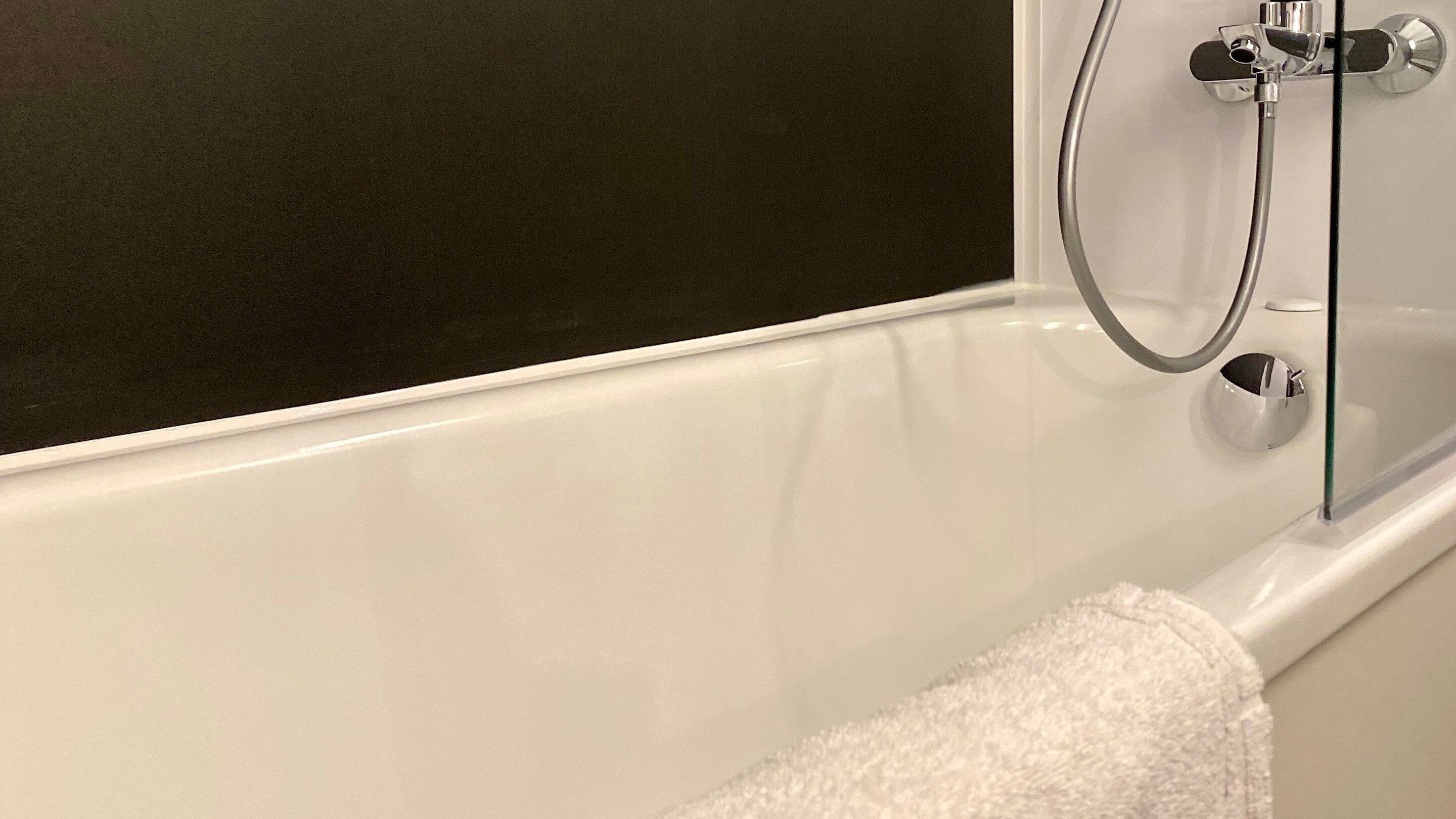 A white bathtub with a glass shower enclosure and a white towel.