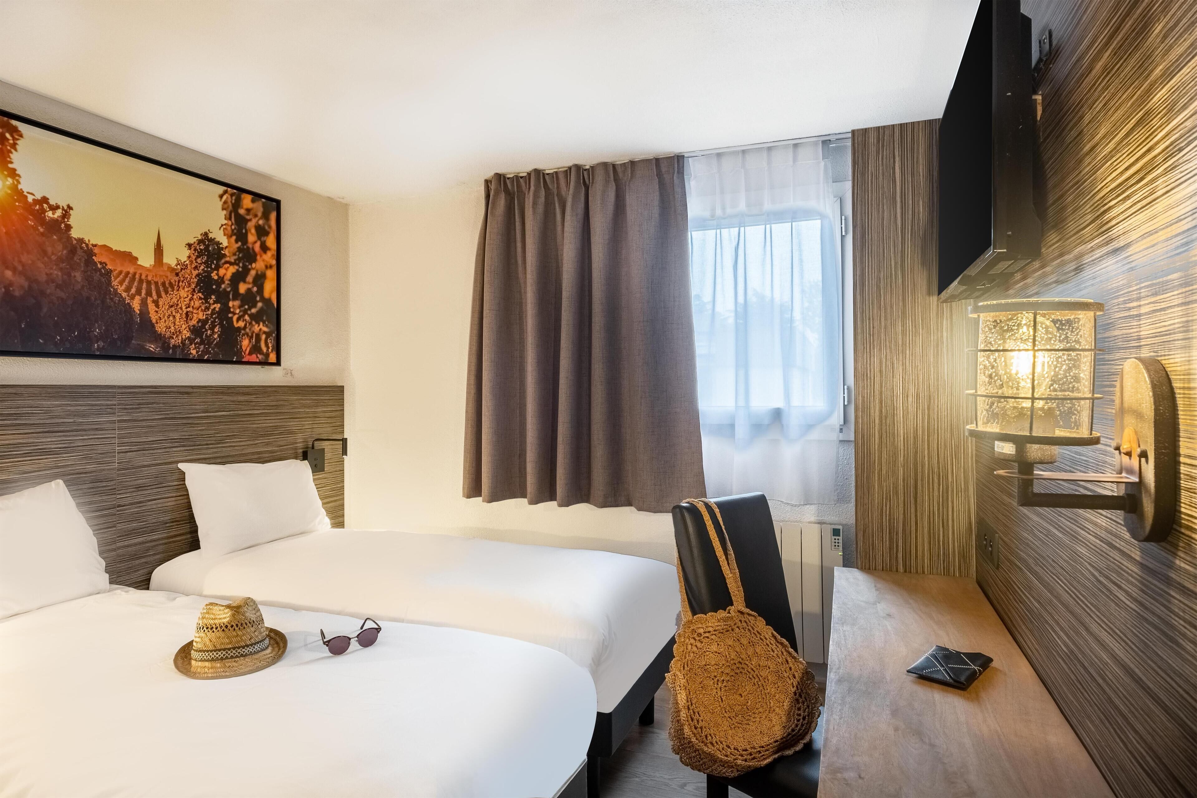 A hotel room with two beds, a large painting, a TV, a wall-mounted light, and a window with curtains.