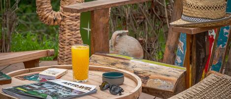 Una terraza de madera con una mesa redonda, un vaso de jugo de naranja, un cuenco y un sombrero.