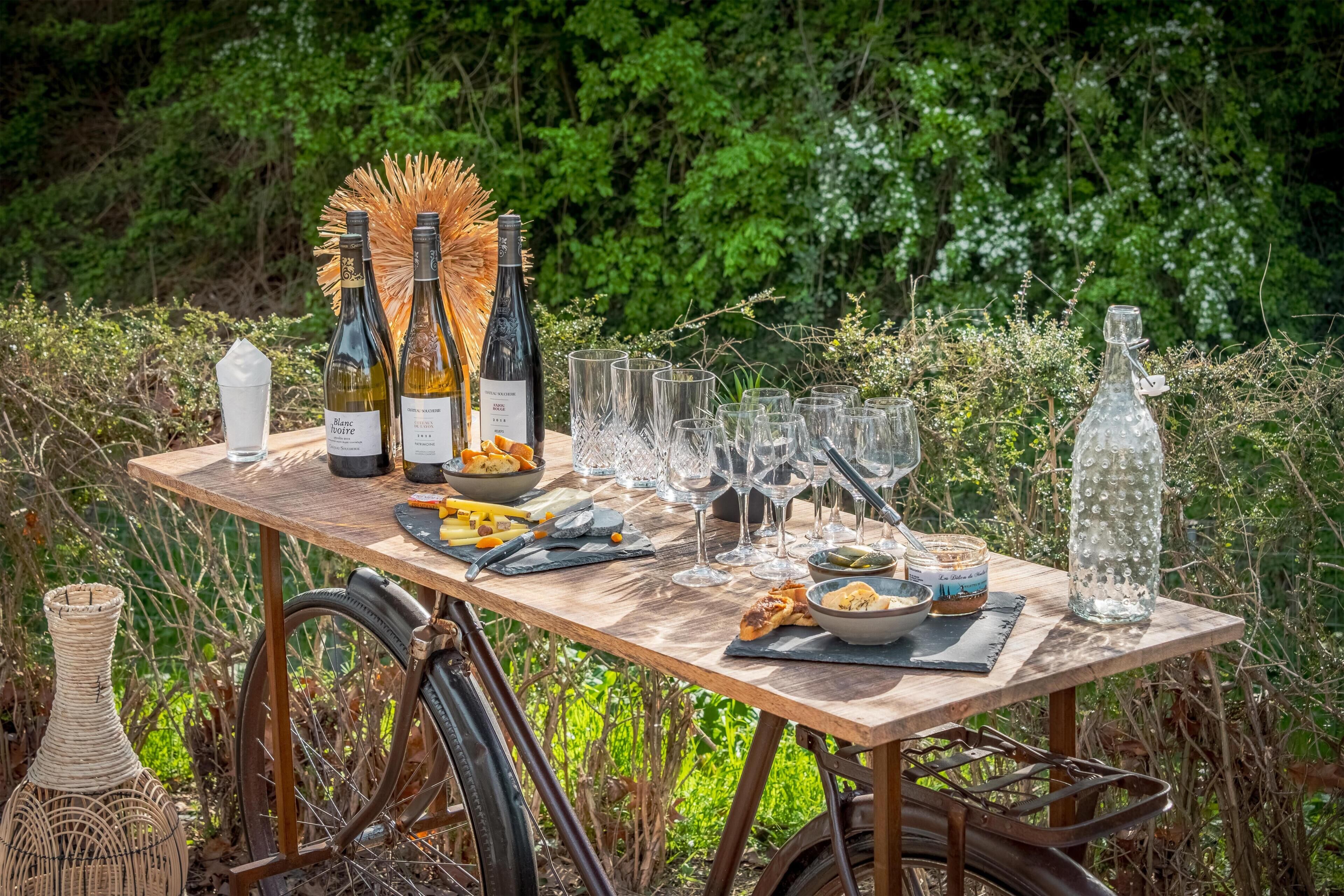 Mobiliario de comedor al aire libre con mesa de madera, botellas de vino, copas y una cesta de mimbre.