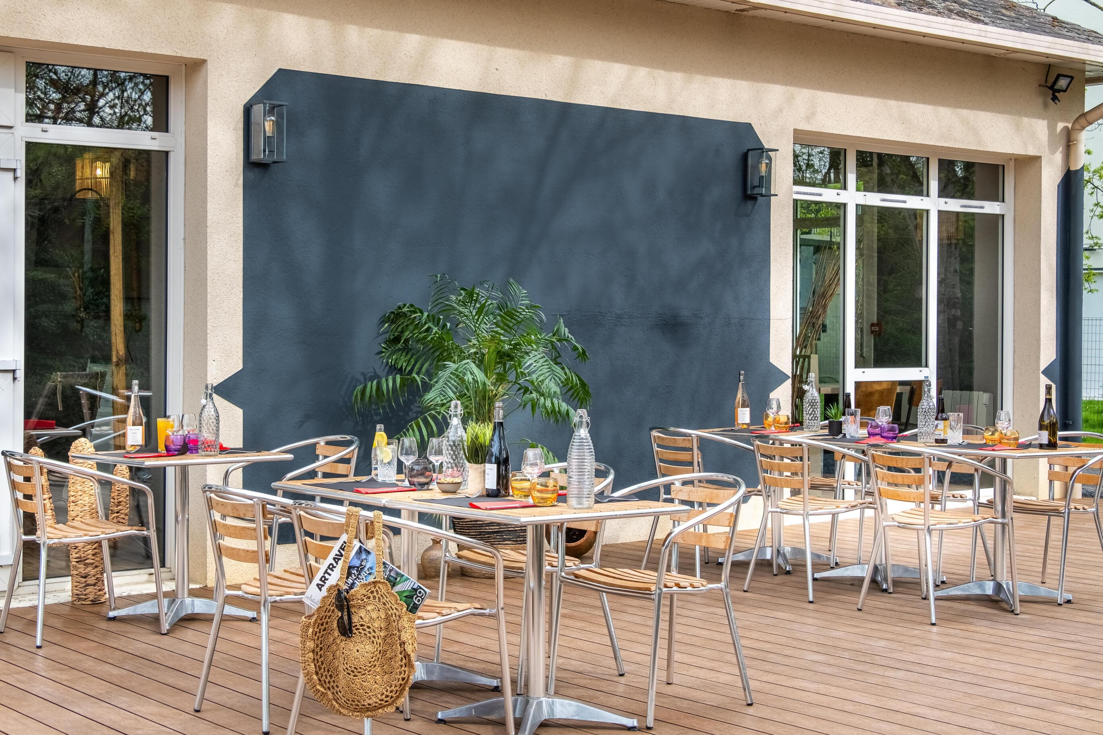 Un patio al aire libre con sillas y mesas de metal, una planta en maceta y botellas de vino.