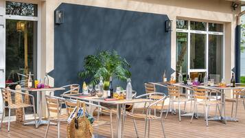 Un patio al aire libre con sillas y mesas de metal, una planta en maceta y botellas de vino.