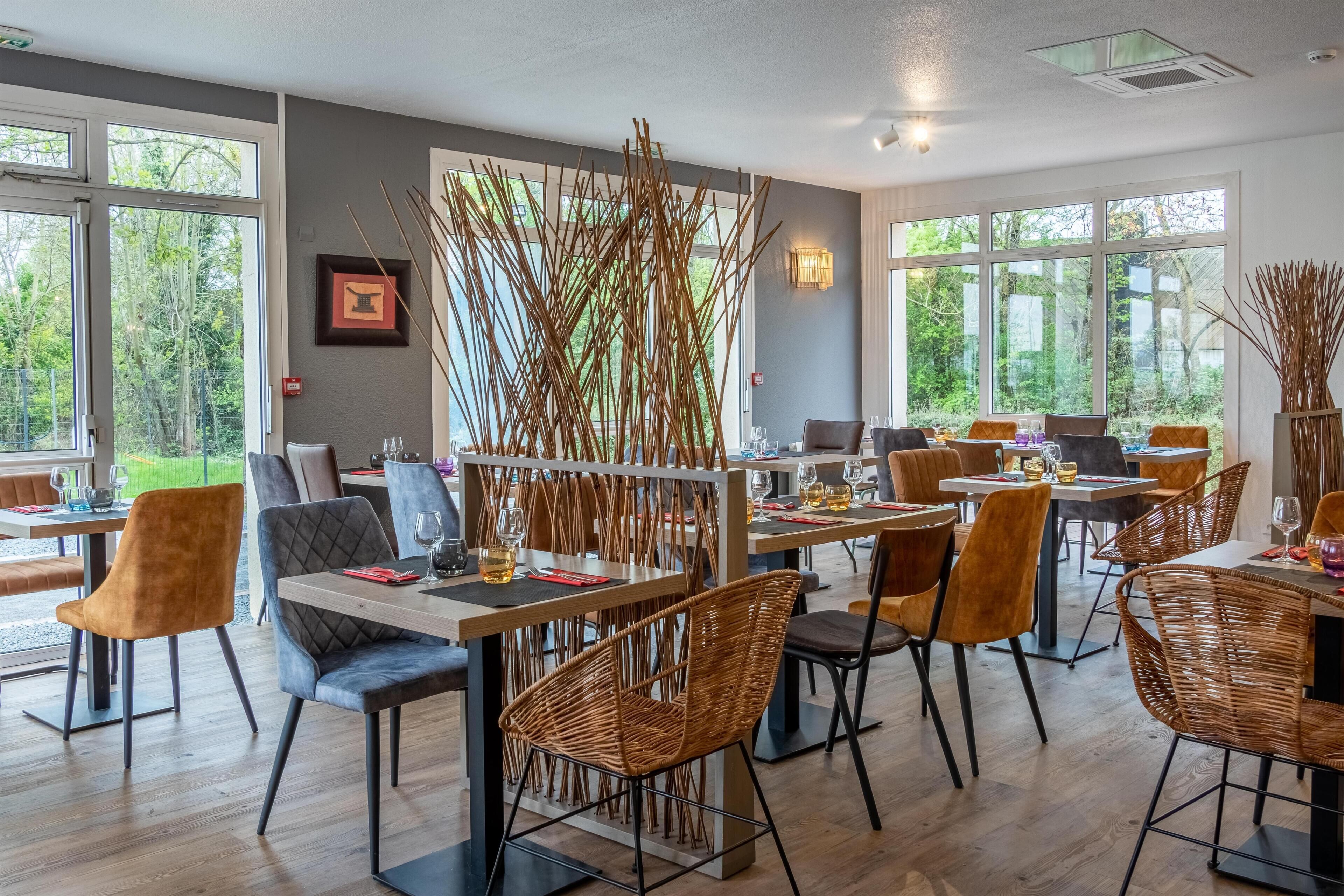 A restaurant with multiple tables and chairs, large windows, and a decorative bamboo wall.