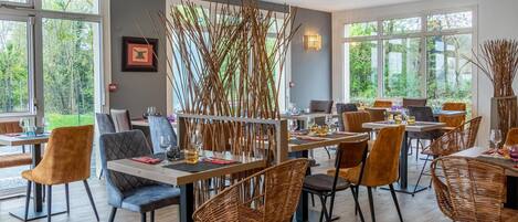 Un restaurante con varias mesas y sillas, ventanas amplias y una pared decorativa de bambú.