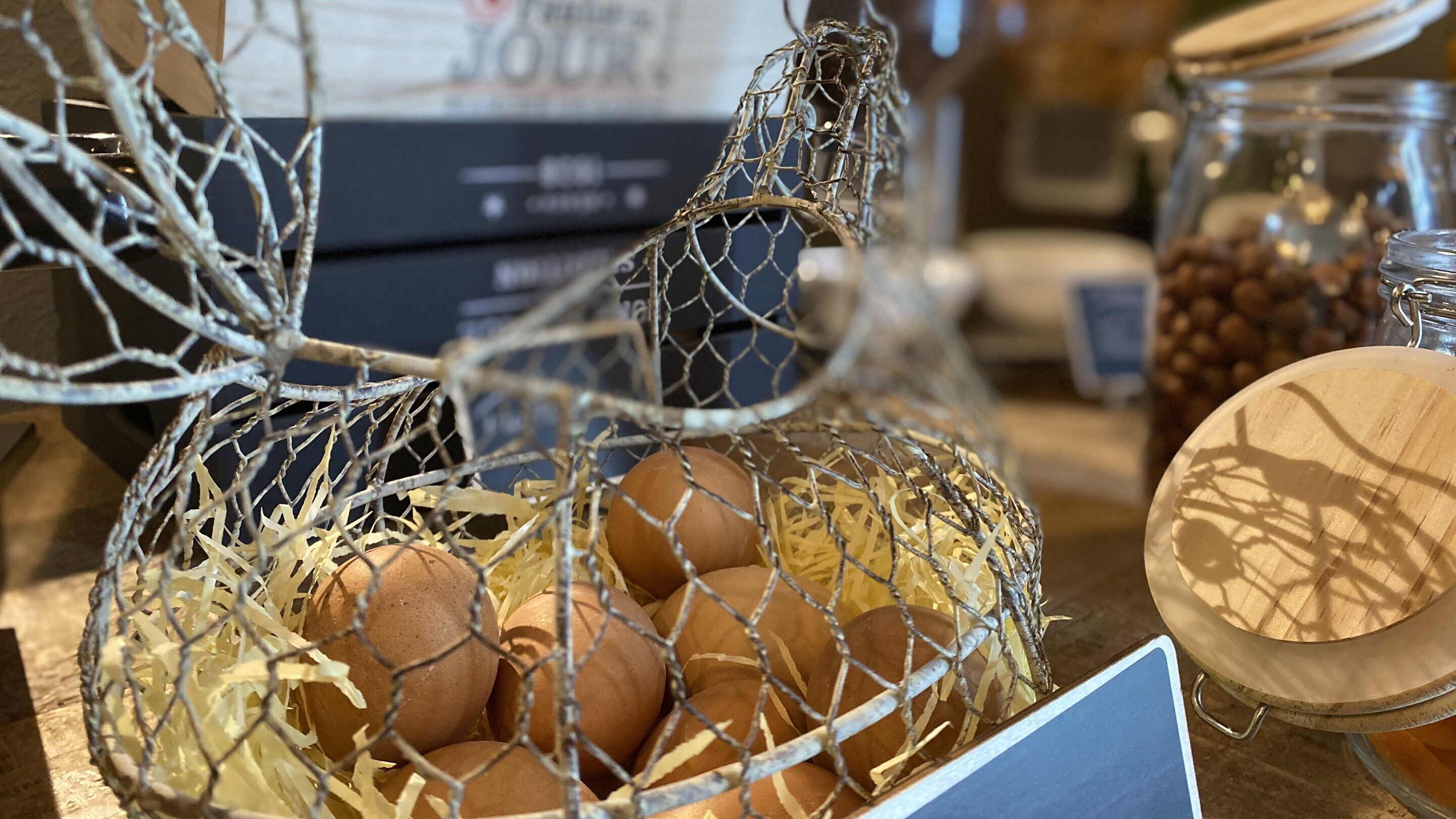 A basket of eggs in a wire basket, with a wooden tray and a jar of coffee beans in the background.