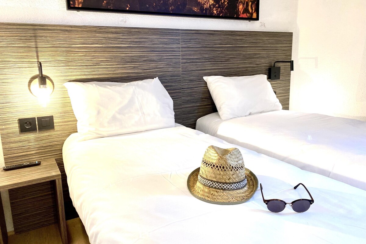 A hotel room with two beds, a nightstand, a wall-mounted TV, and a remote control.