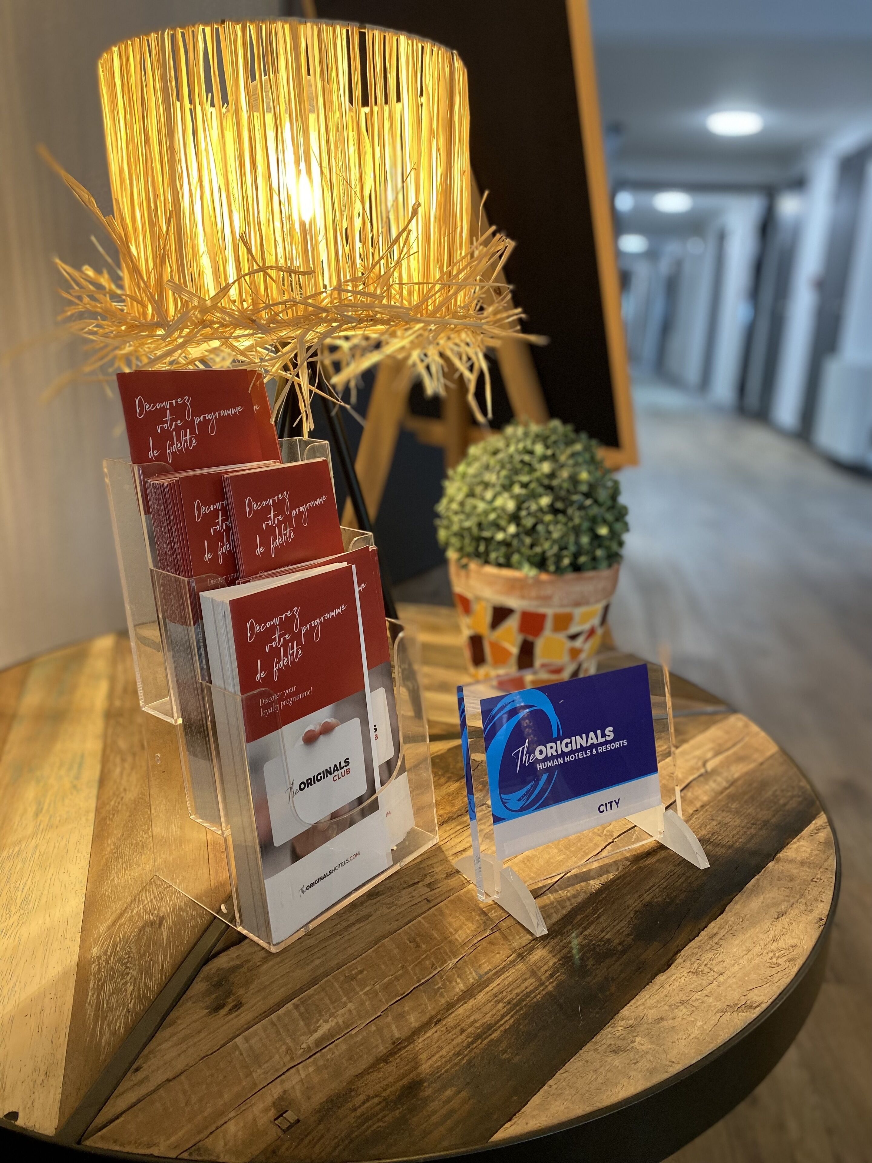A wooden table with a clear acrylic stand holding brochures and a sign for The Originals Hotel & Resorts.