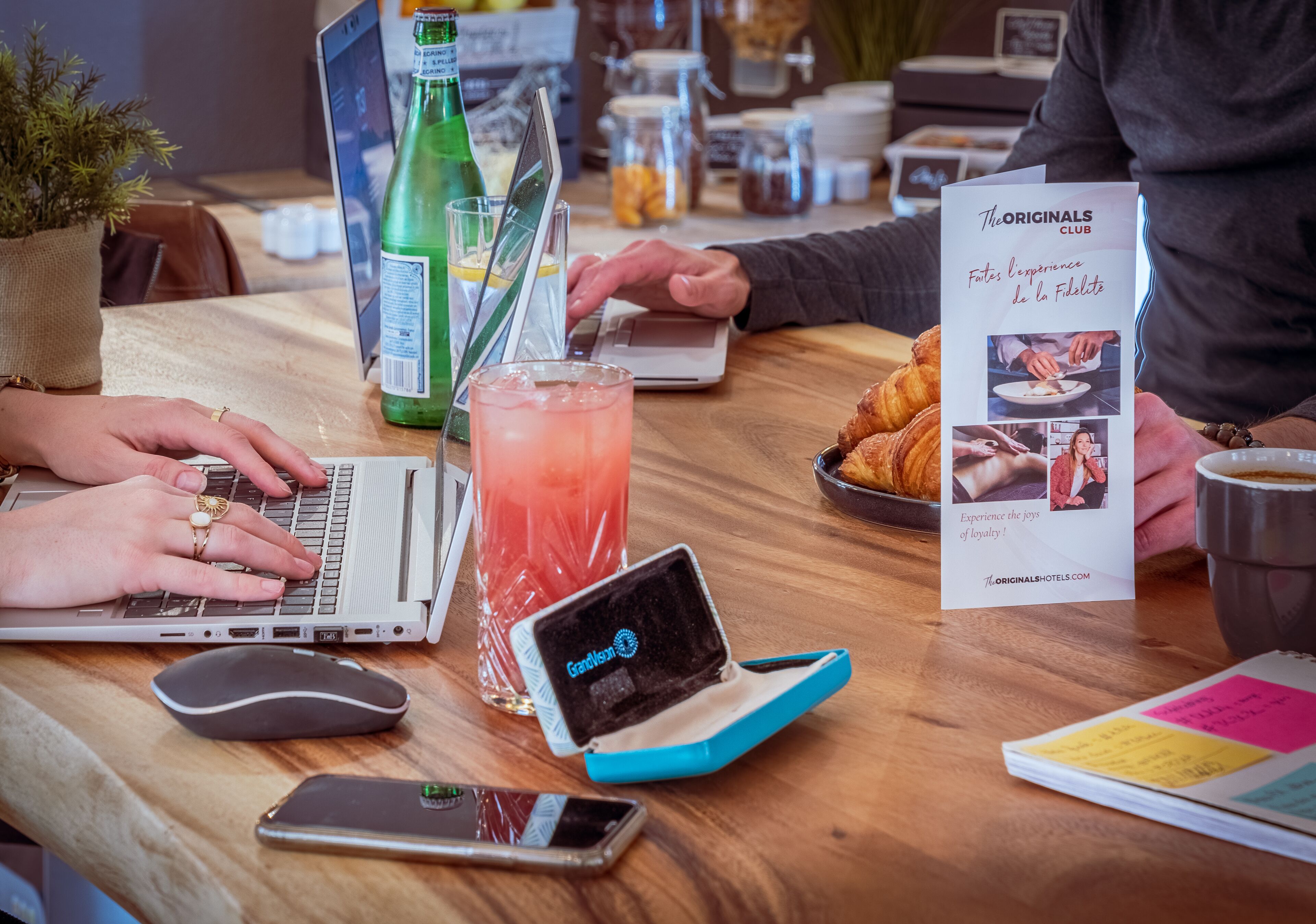 Una mesa de madera con una laptop, un teléfono inteligente, una tablet, una bebida y un folleto.