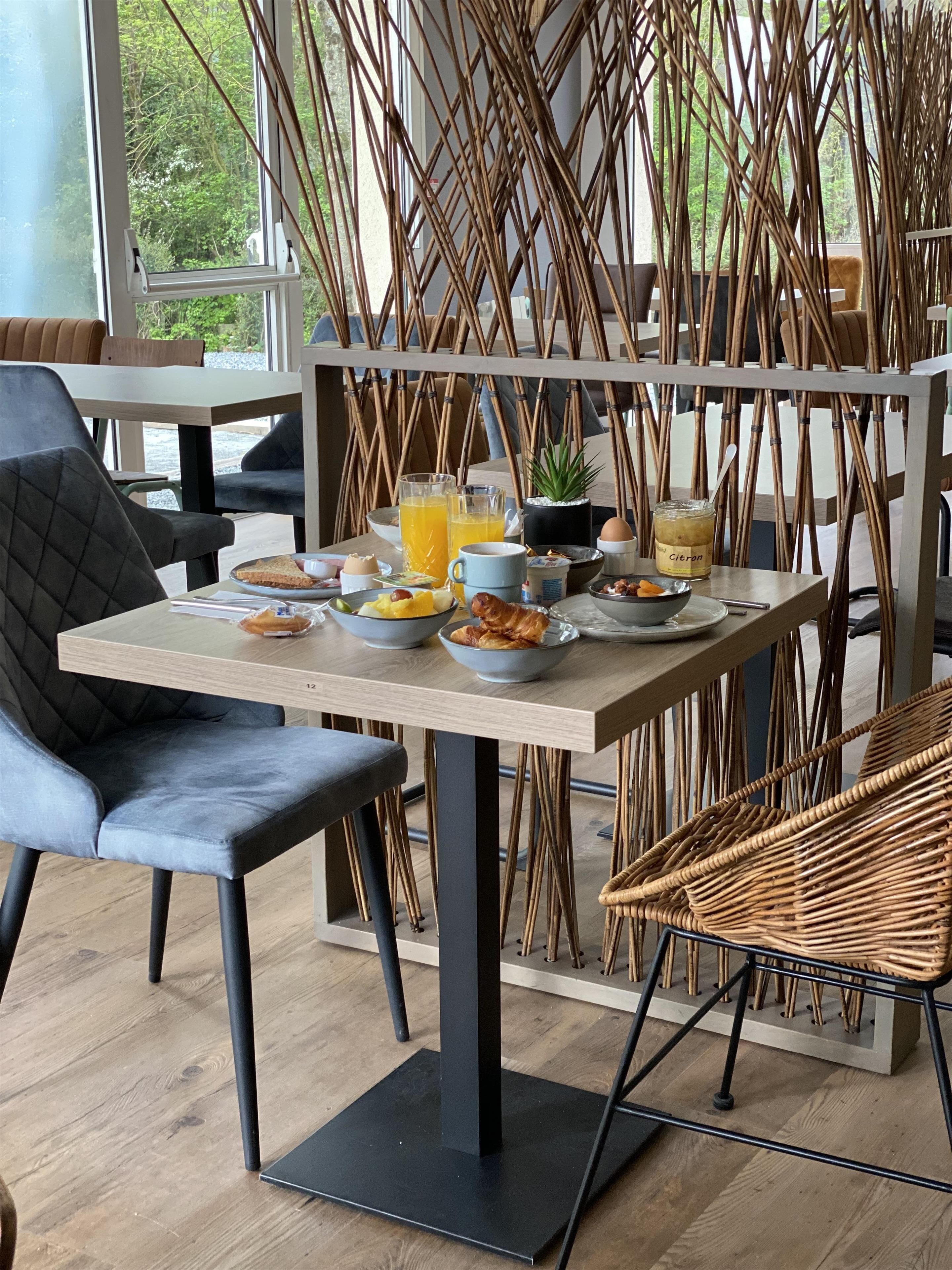 Un comedor con una mesa preparada para el desayuno, que incluye un cuenco de fruta, un croissant y un vaso de zumo de naranja.