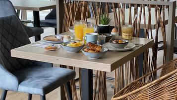 Un comedor con una mesa preparada para el desayuno, que incluye un cuenco de fruta, un croissant y un vaso de zumo de naranja.