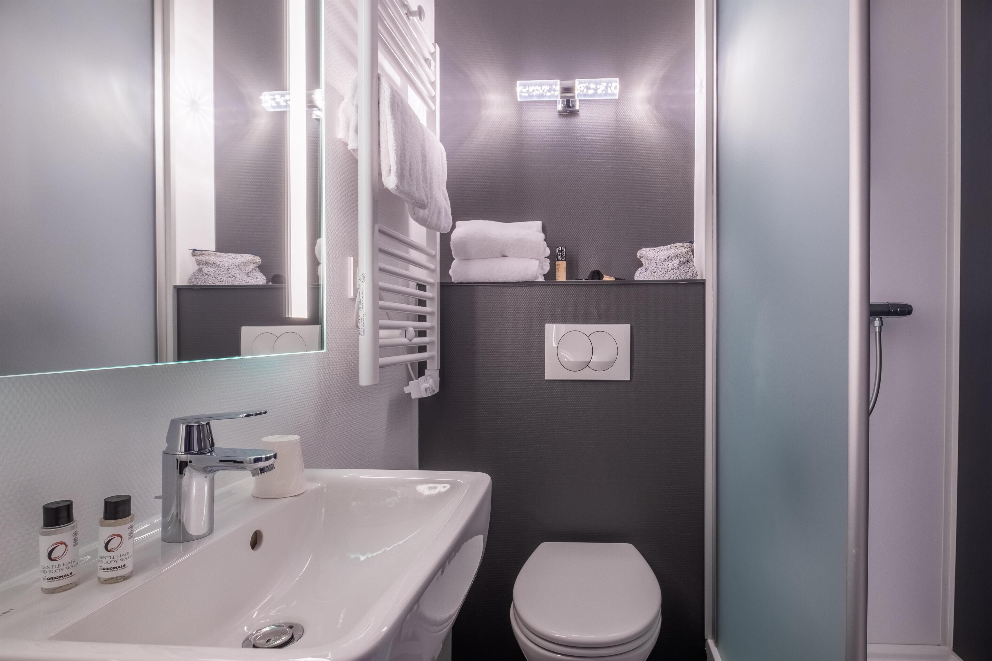 A modern bathroom with a sink, mirror, towel rack, and toilet.