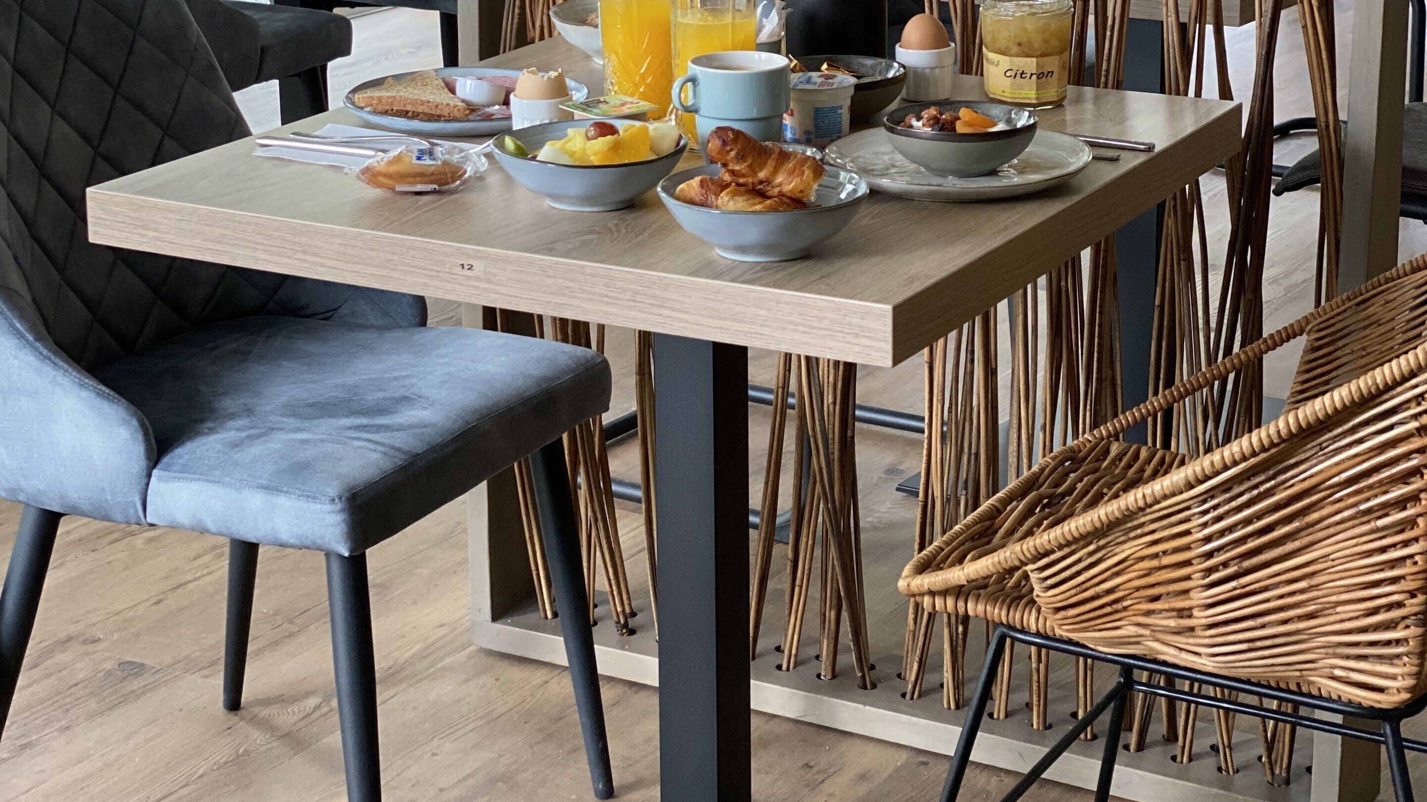 A breakfast table with various food items, a chair, and a wicker chair.