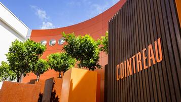 Um edifício com fachada curva, um letreiro de 'Cointreau' em destaque e três árvores na frente.