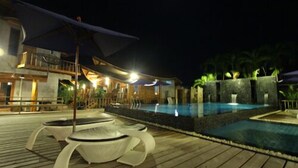 A nighttime resort pool area with lounge chairs, a pool, and a building with a balcony. - Tique Series Boutique Resort (Rayong)