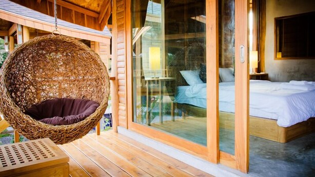 A wooden cabin with a hanging chair, a bed, and a glass door leading to a balcony. - Tique Series Boutique Resort (Rayong)