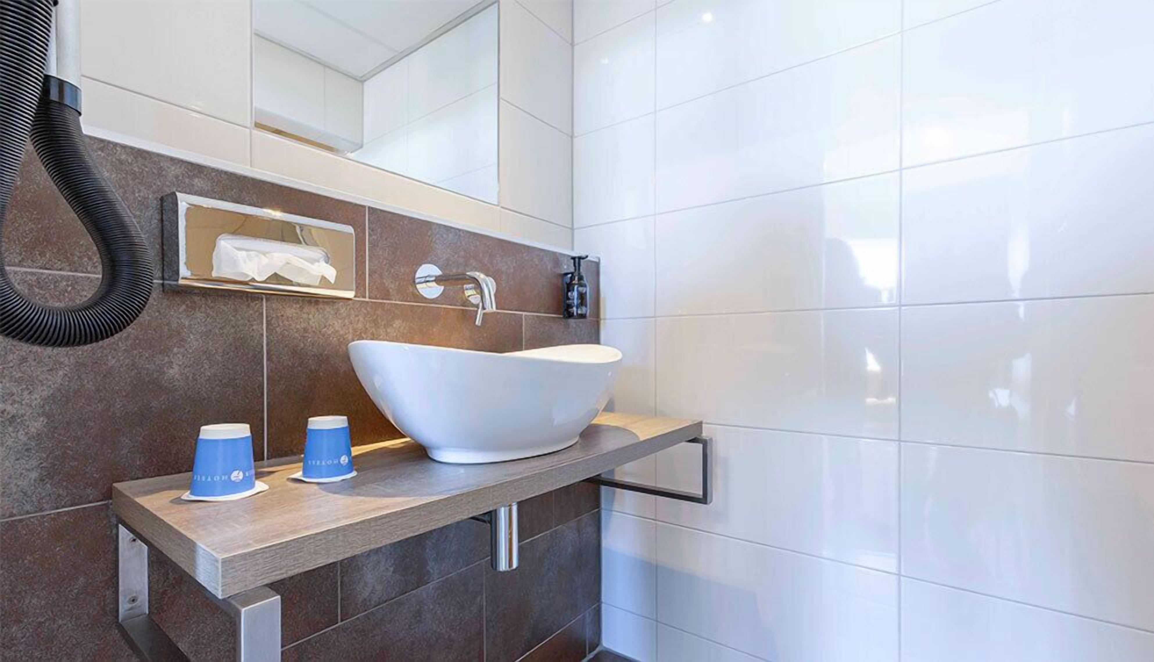 A modern bathroom with a large vessel sink, a towel dispenser, and a mirror.