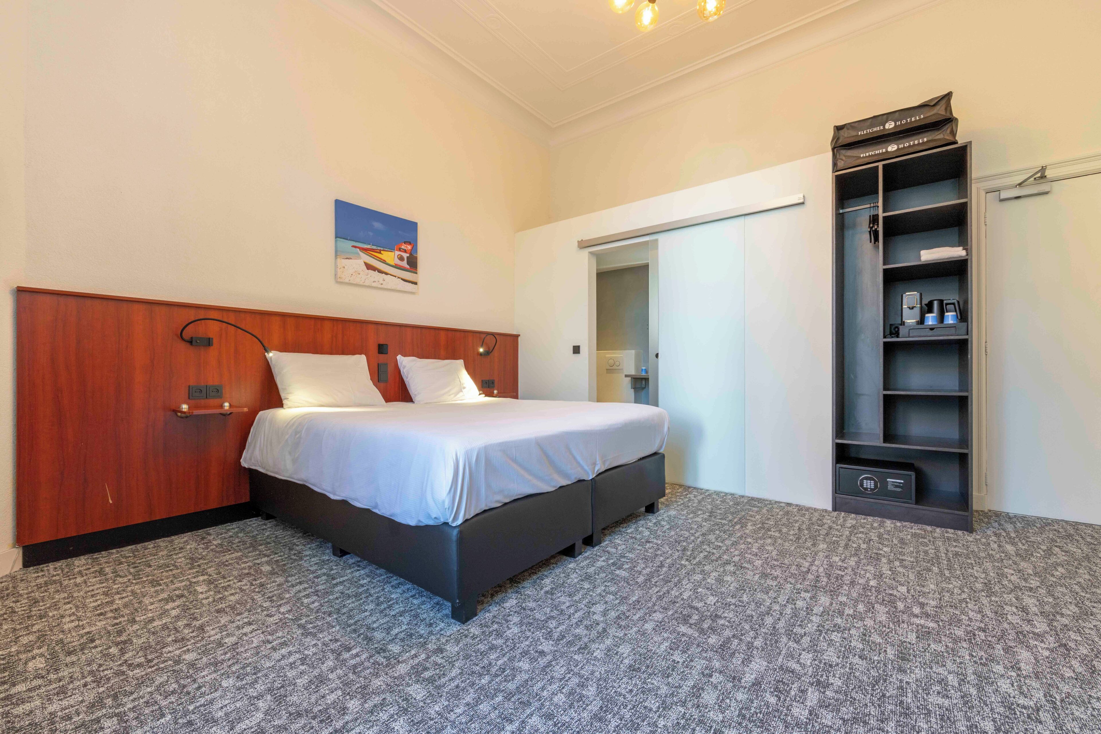 Une chambre d’hôtel avec un lit, une armoire, une étagère avec des articles de toilette et un tableau au mur.