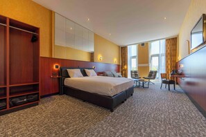 Een hotelkamer met een groot bed, een zithoek met stoelen, een bureau en een kledingkast.