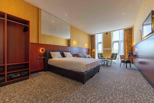 Una habitación de hotel con una cama grande, una zona de estar con sillas, un escritorio y un armario.
