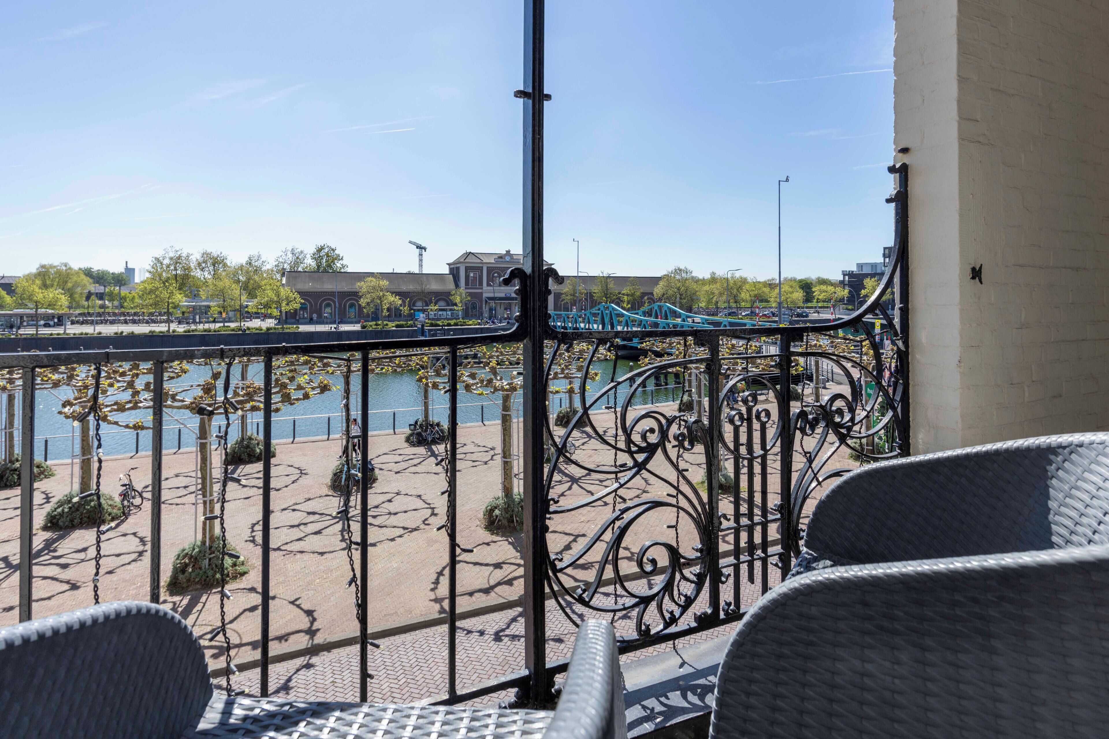 Een balkon met rieten stoelen, uitzicht op een brug en een wateroppervlak.