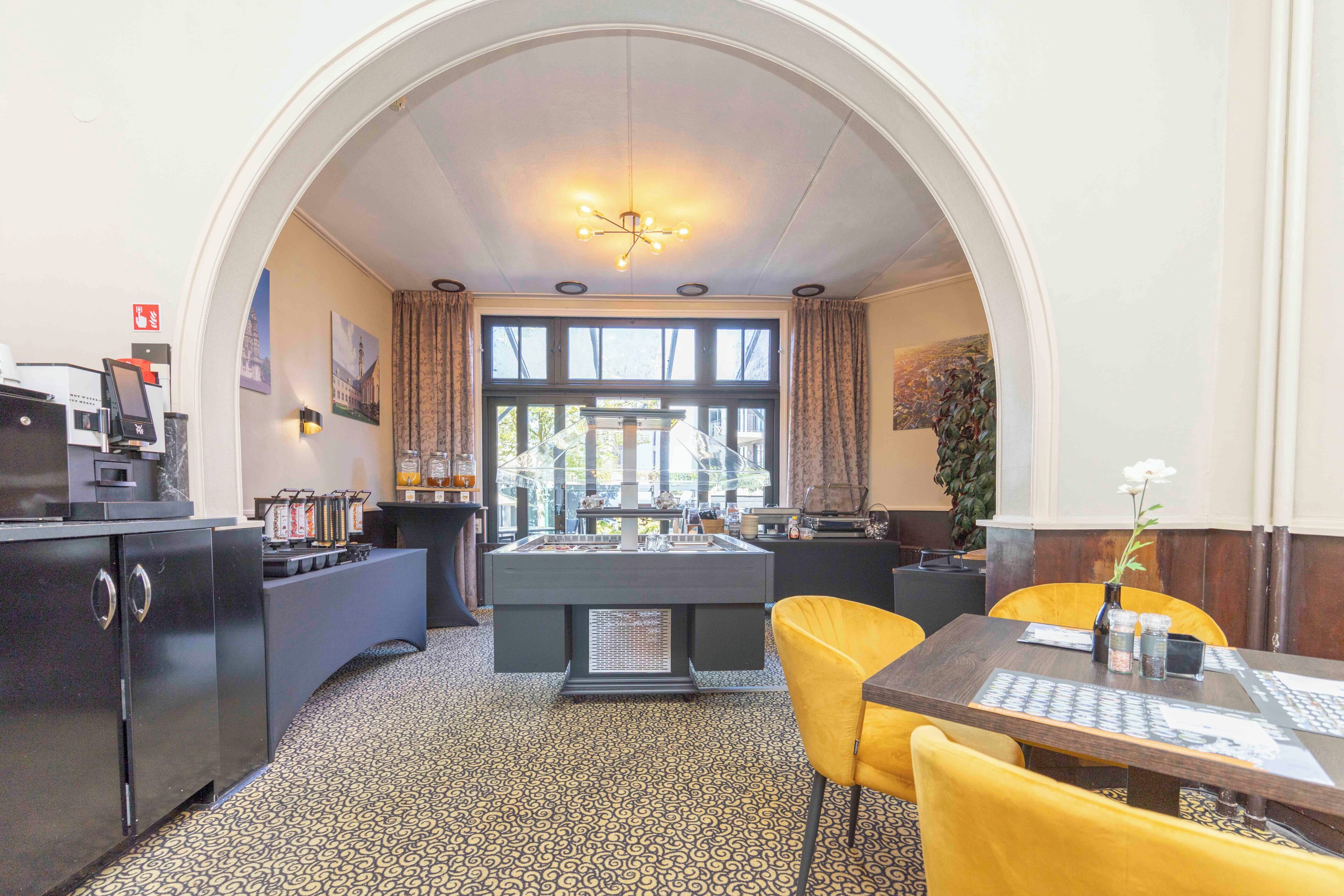 Ein Zimmer mit Billardtisch, einem Esstisch mit gelben Stühlen, einer Kaffeemaschine und einem großen Fenster mit Vorhängen.
