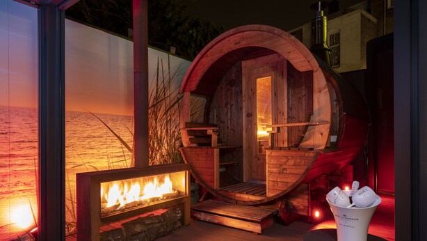 Una habitación con forma de barril de madera, con chimenea y una mesa con vasos.